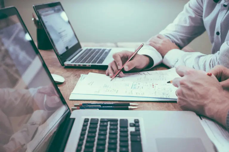 Mains annotant un carnet à côté d'un ordinateur portable, pendant un audit