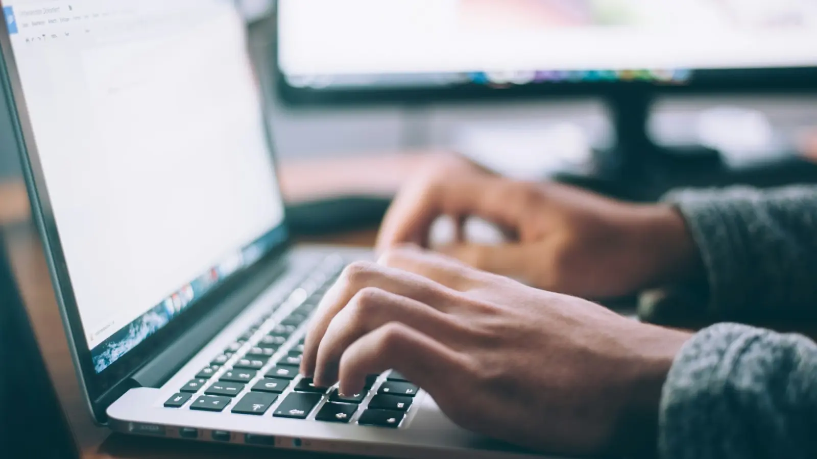 Mains sur le clavier d'un ordinateur portable, écran allumé en arrière-plan