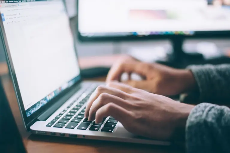 Mains sur le clavier d'un ordinateur portable, écran allumé en arrière-plan